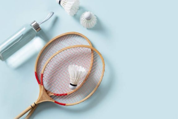 Badminton Accessories Two badminton rackets, shuttlecock, and a sports bottle on a light blue surface.